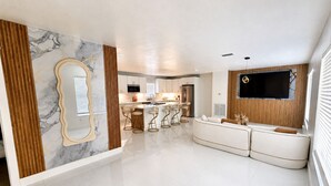 A modern kitchen with a marble backsplash, a central island with bar stools, and a built-in TV. - Elegant 4BR Retreat Near Tampa with Private Office (Brandon)