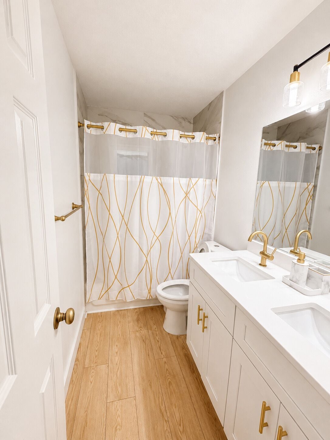 A bathroom with a white vanity, gold fixtures, and a shower curtain with a gold pattern.