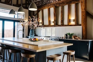Una cocina moderna con una isla grande, taburetes de bar, iluminación colgante y un jarrón con flores.