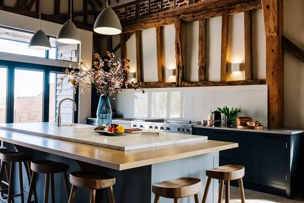 A modern kitchen with a large island, bar stools, pendant lighting, and a vase of flowers.