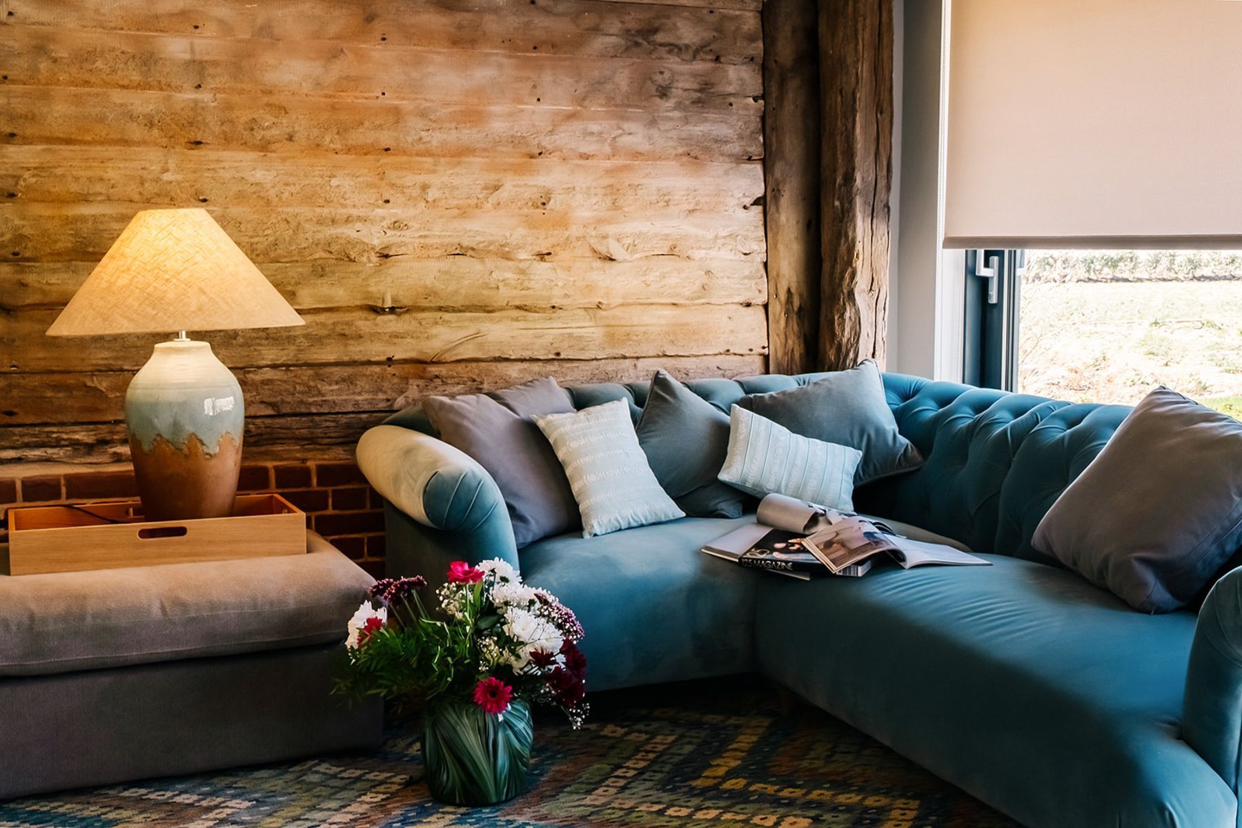 Une pièce chaleureuse avec un mur en bois, un canapé bleu, une petite table en bois avec une lampe et un vase rempli de fleurs.