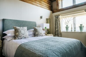 A neatly made bed with patterned pillows, a bedside lamp, and a window with decorative vases. - Pheasant Barn - Six Bedroom Villa, Sleeps 12 (Brome)
