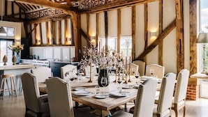 A dining area with a wooden table set for a meal, surrounded by chairs, in a room with exposed wooden beams and brick walls.