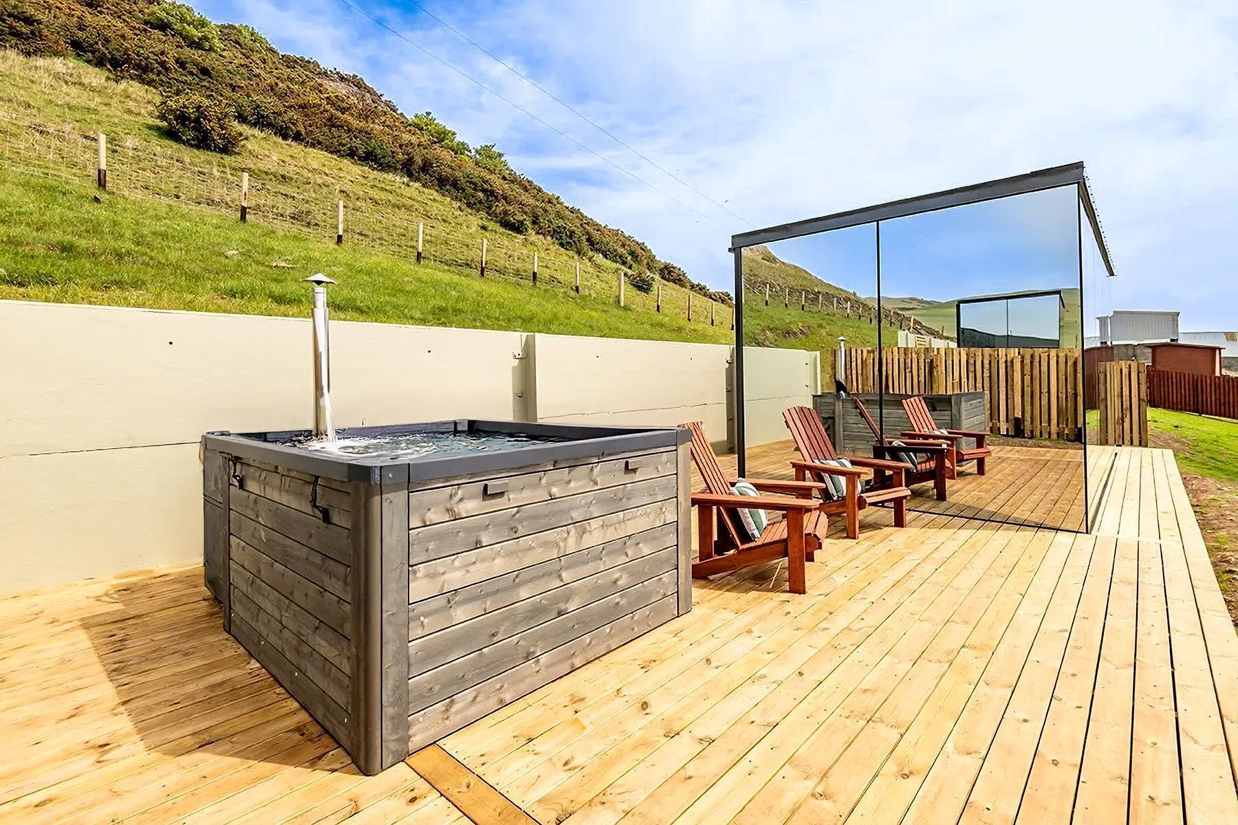 An outdoor deck with a hot tub, wooden chairs, and a wooden fence.