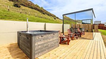 An outdoor deck with a hot tub, wooden chairs, and a wooden fence.