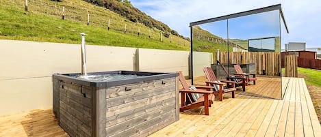 An outdoor deck with a hot tub, wooden chairs, and a wooden fence.