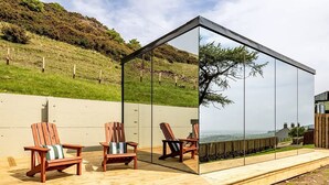 Un espace extérieur moderne, aménagé avec des chaises en bois et doté d’une structure vitrée qui reflète le paysage environnant.
