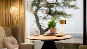Un salon moderne avec une table ronde, un canapé, une plante en pot, une lampe et une vue sur un arbre à travers une fenêtre.