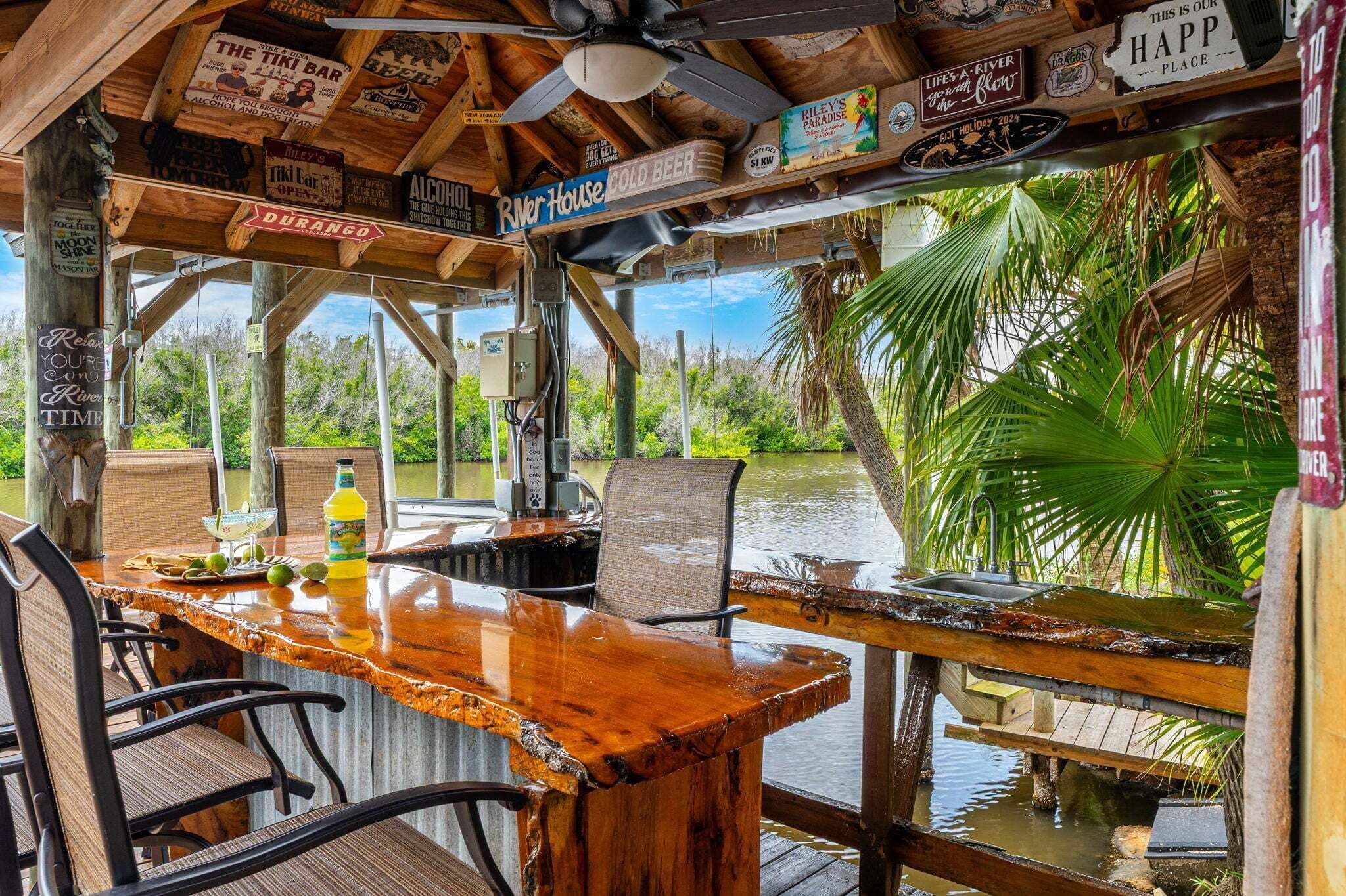 A wooden bar with chairs, a bottle of drink, and a view of a river.