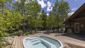Un bain à remous entouré d’une terrasse en bois, de sièges d’extérieur et d’un mur en pierre.