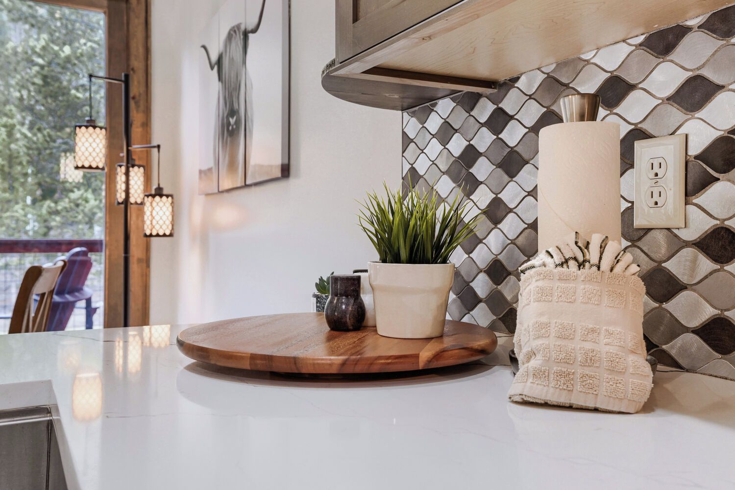 Una cocina moderna con encimera blanca, tabla de madera, planta en maceta y toalla decorativa.