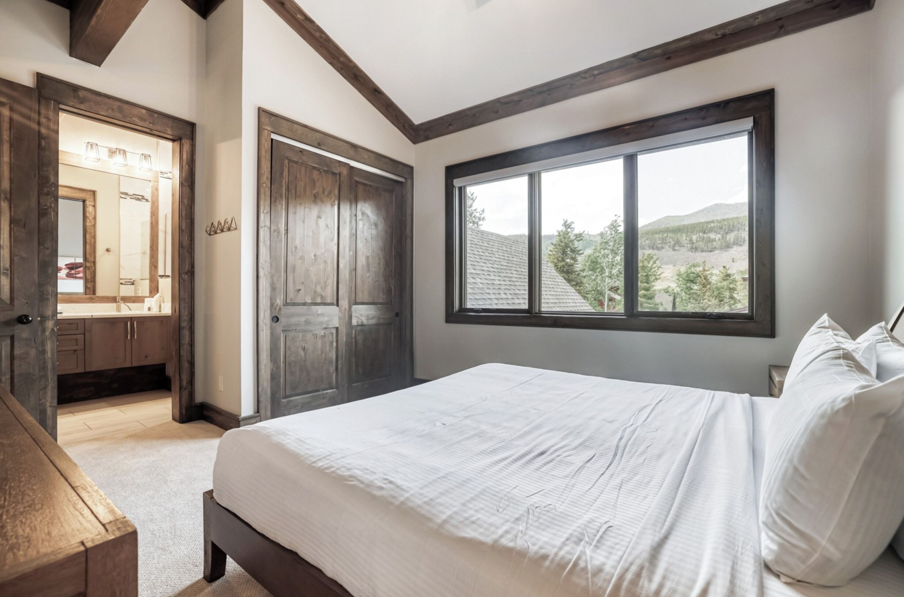 Un dormitorio con una ventana grande, una puerta de madera y una cama con sábanas blancas.
