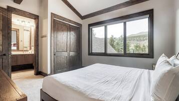 Un dormitorio con una ventana grande, una puerta de madera y una cama con sábanas blancas.