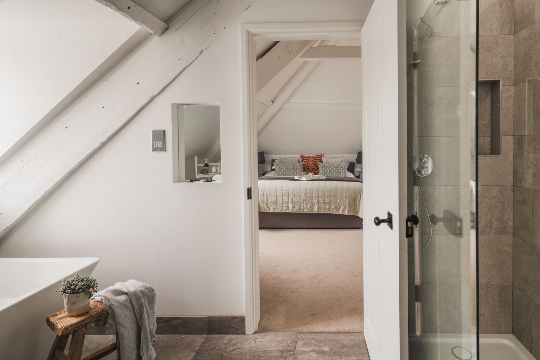 Une chambre à coucher avec un lit, une table de chevet ornée d’une plante, un miroir, et une salle de bain équipée d’une douche et d’une baignoire.