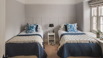A bedroom with two beds, a nightstand, a lamp, and a window with curtains.