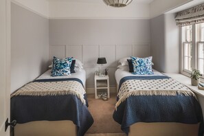 Un dormitorio con dos camas, una mesita de noche, una lámpara y una ventana con cortinas.