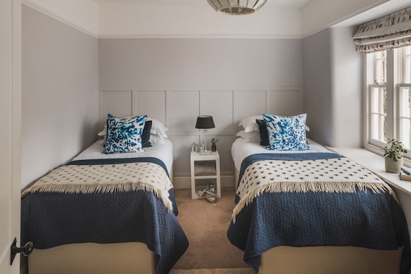 Une chambre avec deux lits, une table de chevet, une lampe et une fenêtre avec des rideaux.