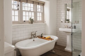Een badkamer met een vrijstaand bad, een raam met zonwering en een douchecabine van glas.