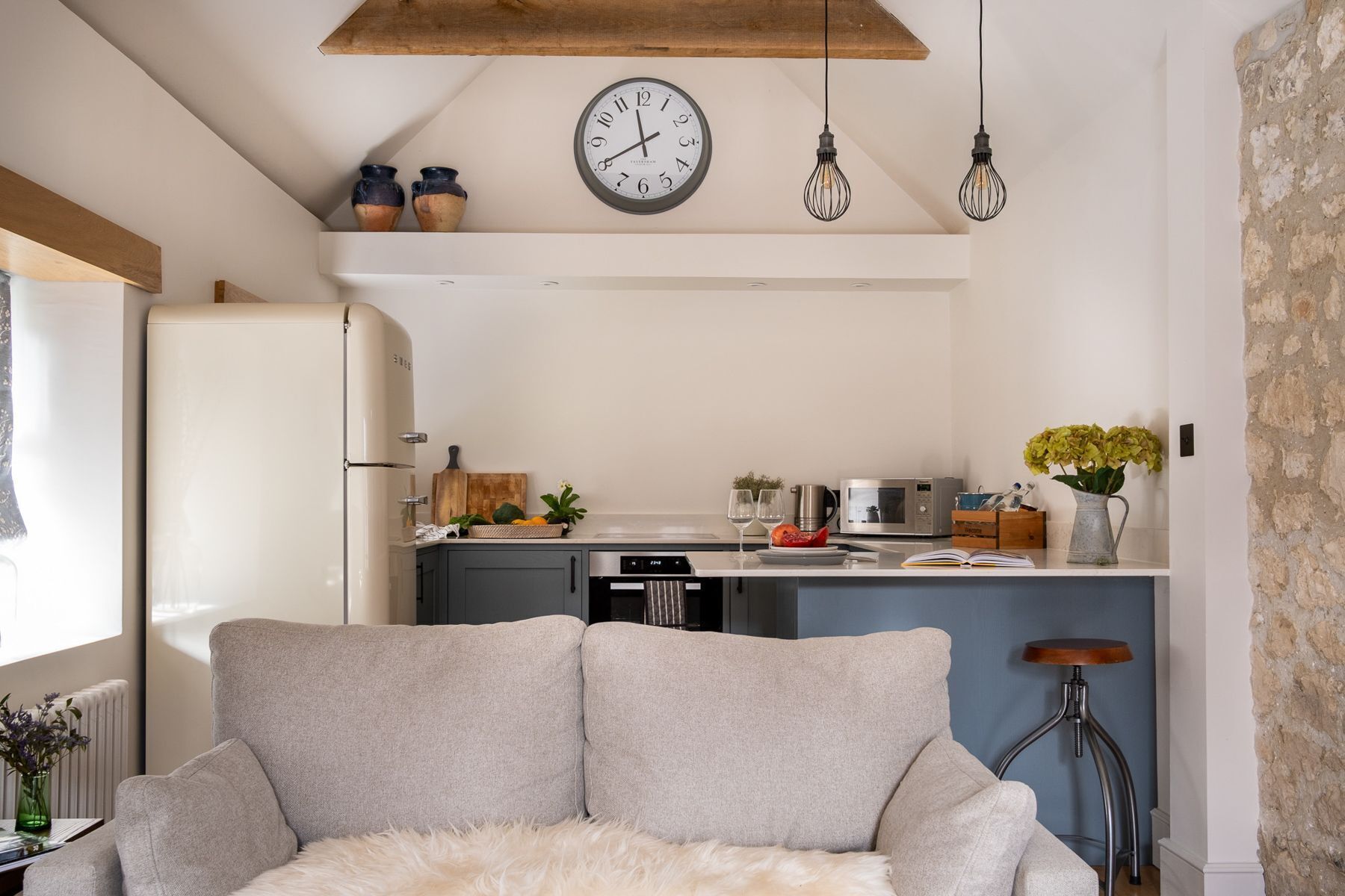 A modern kitchen with a central island, a dining area with a sofa, and a rustic stone wall.