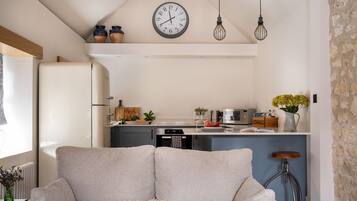A modern kitchen with a central island, a dining area with a sofa, and a rustic stone wall.