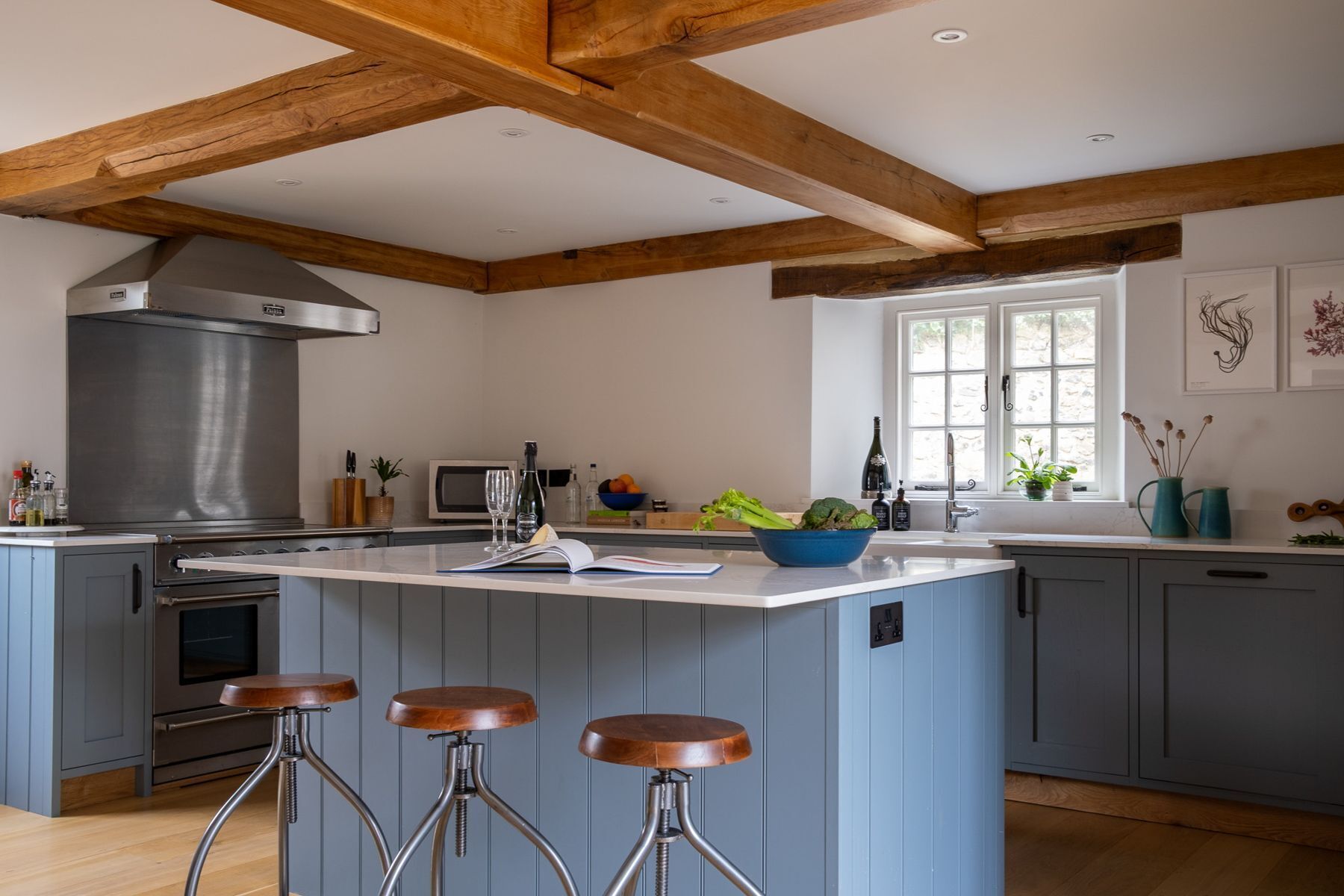 Een keuken met een centraal eiland, barkrukken, een ingebouwde oven en een groot raam.