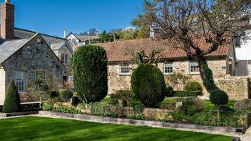 A stone house with a tiled roof, surrounded by well-maintained gardens and a clear blue sky.