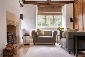 Una sala de estar acogedora con chimenea, un sofá, un sillón y un ventanal con vistas a la vegetación.