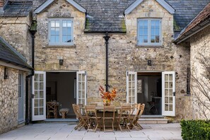 A stone building with two open doors, a table with chairs, and a vase with flowers.