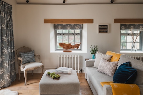 A cozy living room with a wooden-framed window, a rustic chair, a sofa with patterned cushions, and a decorative wooden sculpture.