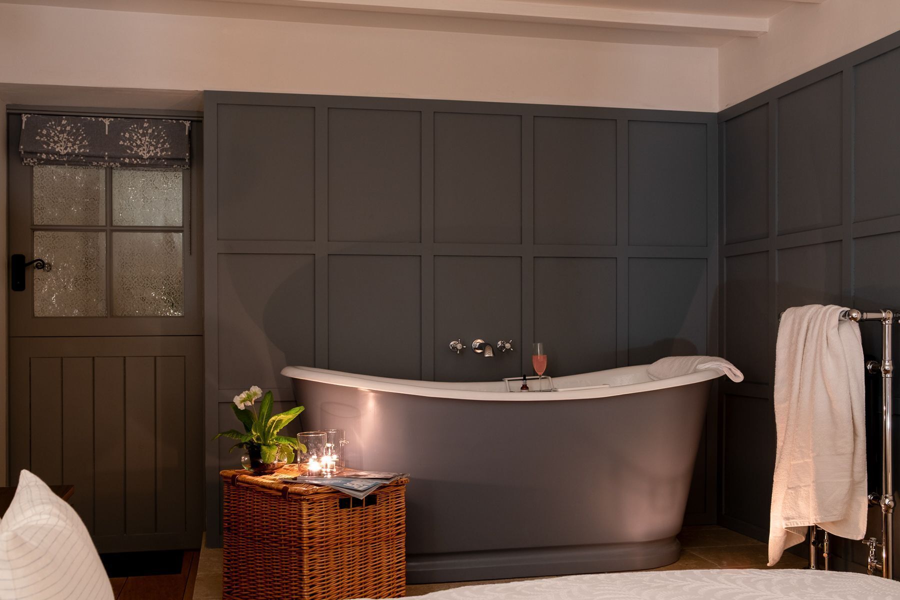 A bathroom with a freestanding bathtub, a wicker basket with candles, and a towel rack.