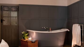A bathroom with a freestanding bathtub, a wicker basket with candles, and a towel rack.