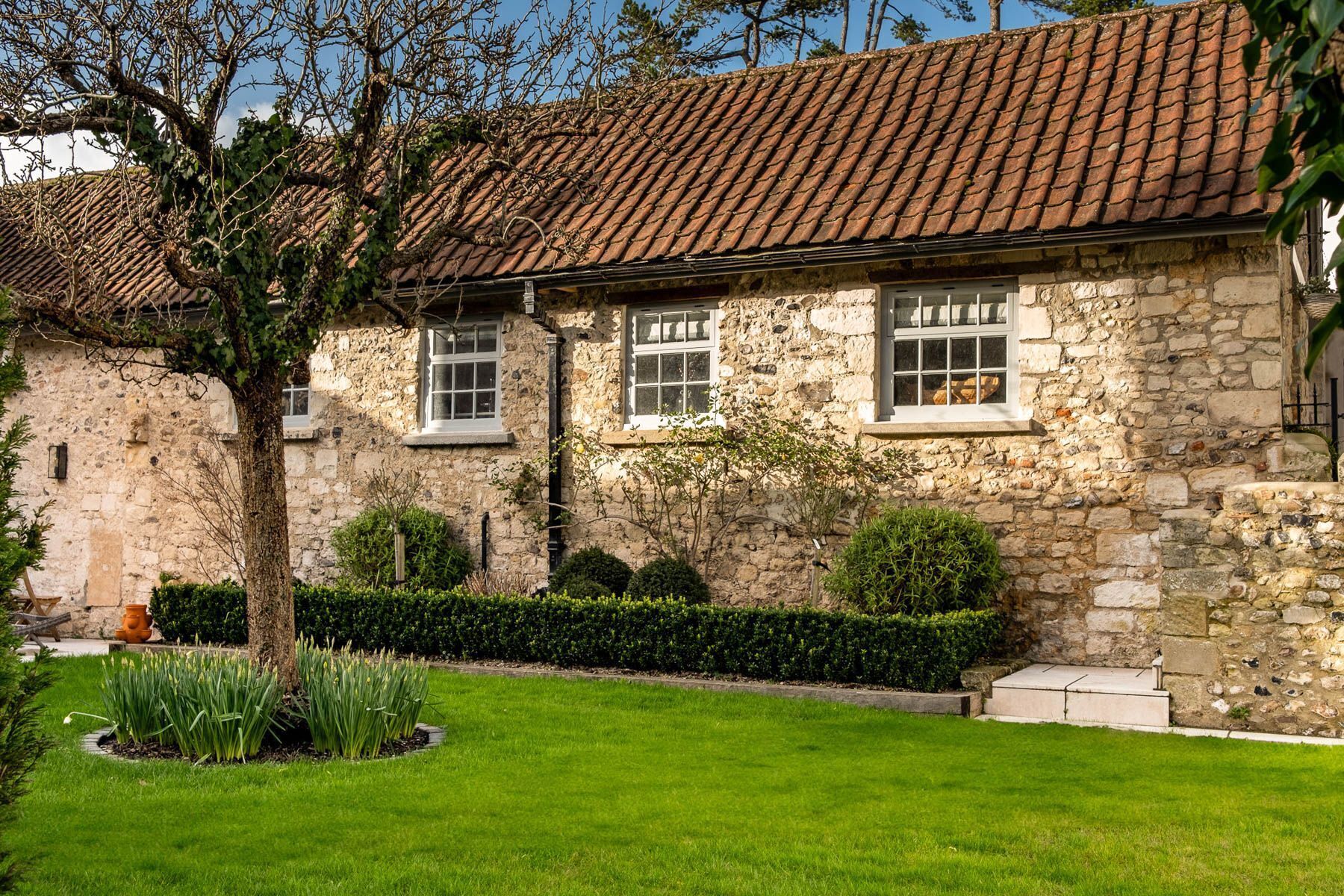 A stone building with a tiled roof, a well-maintained lawn, and a hedge.