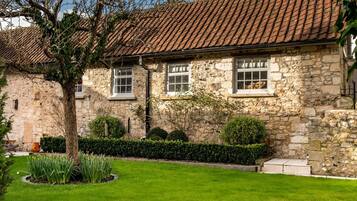A stone building with a tiled roof, a well-maintained lawn, and a hedge.
