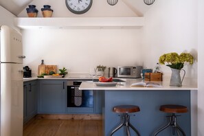 A modern kitchen with a central island, bar stools, a coffee machine, and a microwave.