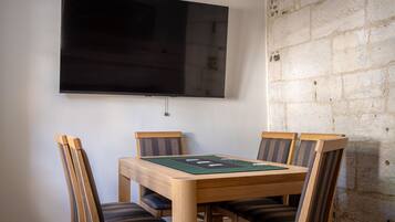 A dining area with a wooden table and chairs, a flat-screen TV mounted on the wall, and a stone wall.