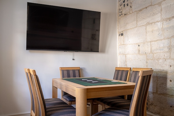 A dining area with a wooden table and chairs, a flat-screen TV mounted on the wall, and a stone wall.