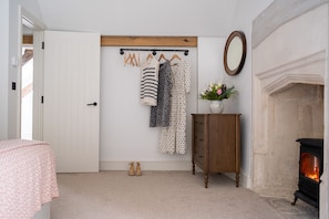 A room with a white door, a wooden coat rack with clothes, a small cabinet with a vase, and a fireplace.