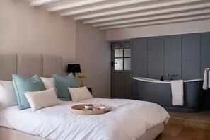 A bedroom with a large bed, a bedside table with a lamp, and a view of a bathroom with a bathtub and sink.