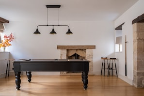 A billiards table in a room with a stone fireplace, wooden beams, and a hanging light fixture.