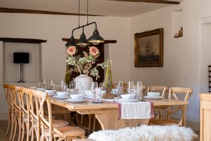Comedor con mesa de madera dispuesta para una comida, rodeada de sillas de madera, un florero y un cuadro en la pared.