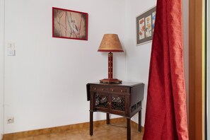 Una stanza con un tavolino in legno, una lampada, una tenda rossa e due opere d'arte incorniciate appese al muro.