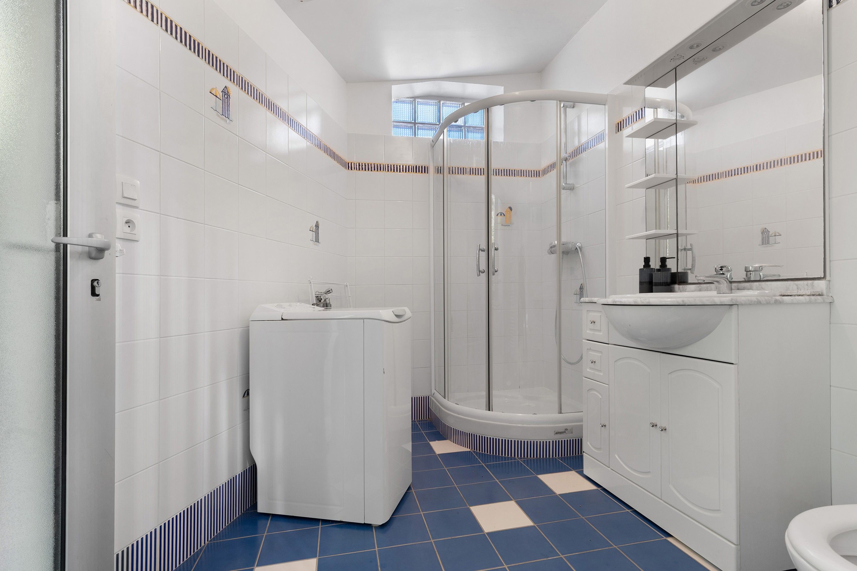 Ein Badezimmer mit weißen Fliesen, einem blau-weißen Schachfußboden, einer Dusche, einem Waschbecken und einem Spiegel.