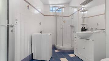 Ein Badezimmer mit weißen Fliesen, einem blau-weißen Schachfußboden, einer Dusche, einem Waschbecken und einem Spiegel.