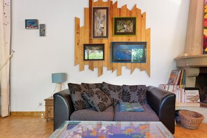 Un salon avec un canapé, une table basse et une cheminée. Les murs sont ornés de tableaux encadrés et une bibliothèque remplie de livres se trouve dans la pièce.