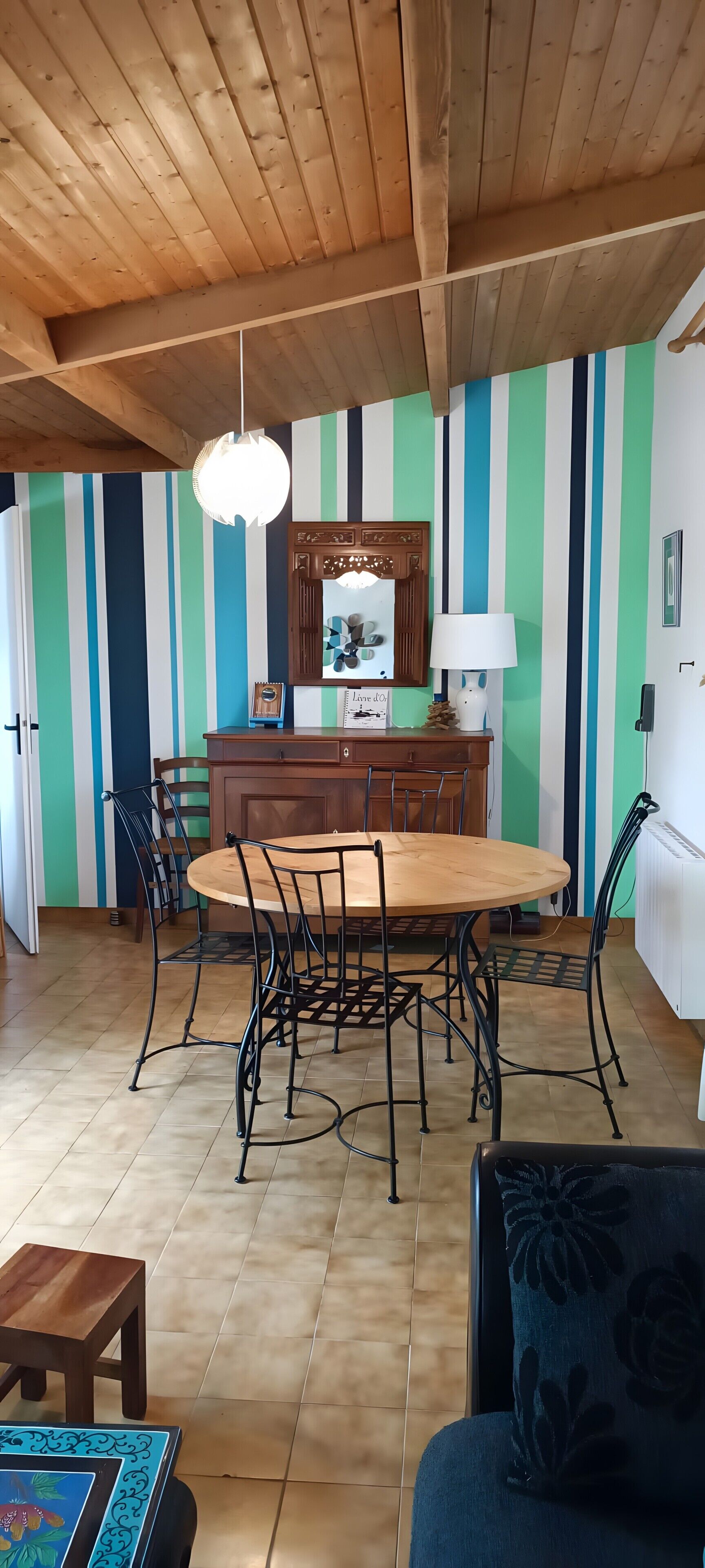A dining area with a wooden table, chairs, a hanging light fixture, and a striped wall.