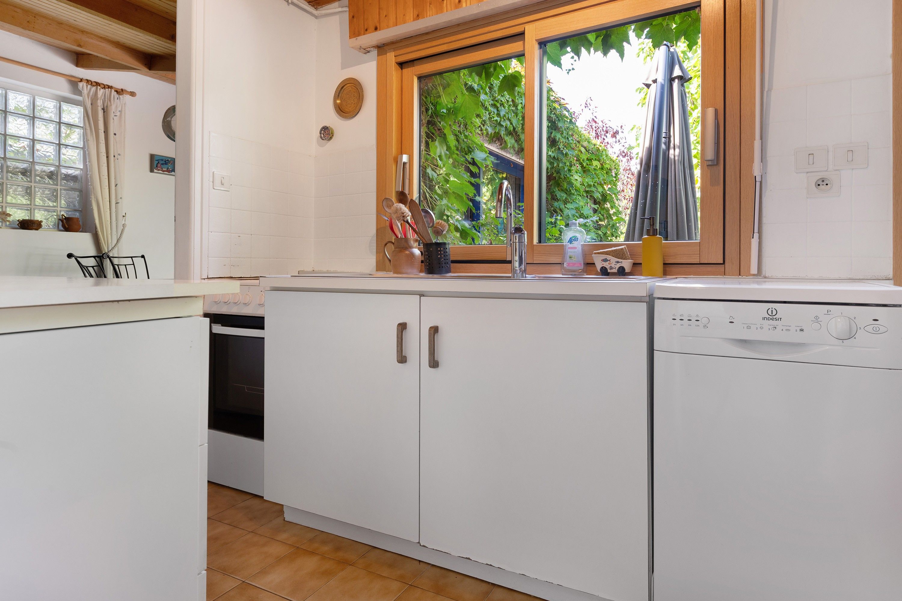 Una cucina con mobili bianchi, una lavastoviglie e una finestra vista verde.