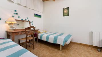 A room with a wooden desk, a chair, two beds with striped bedding, a lamp, and a painting on the wall.
