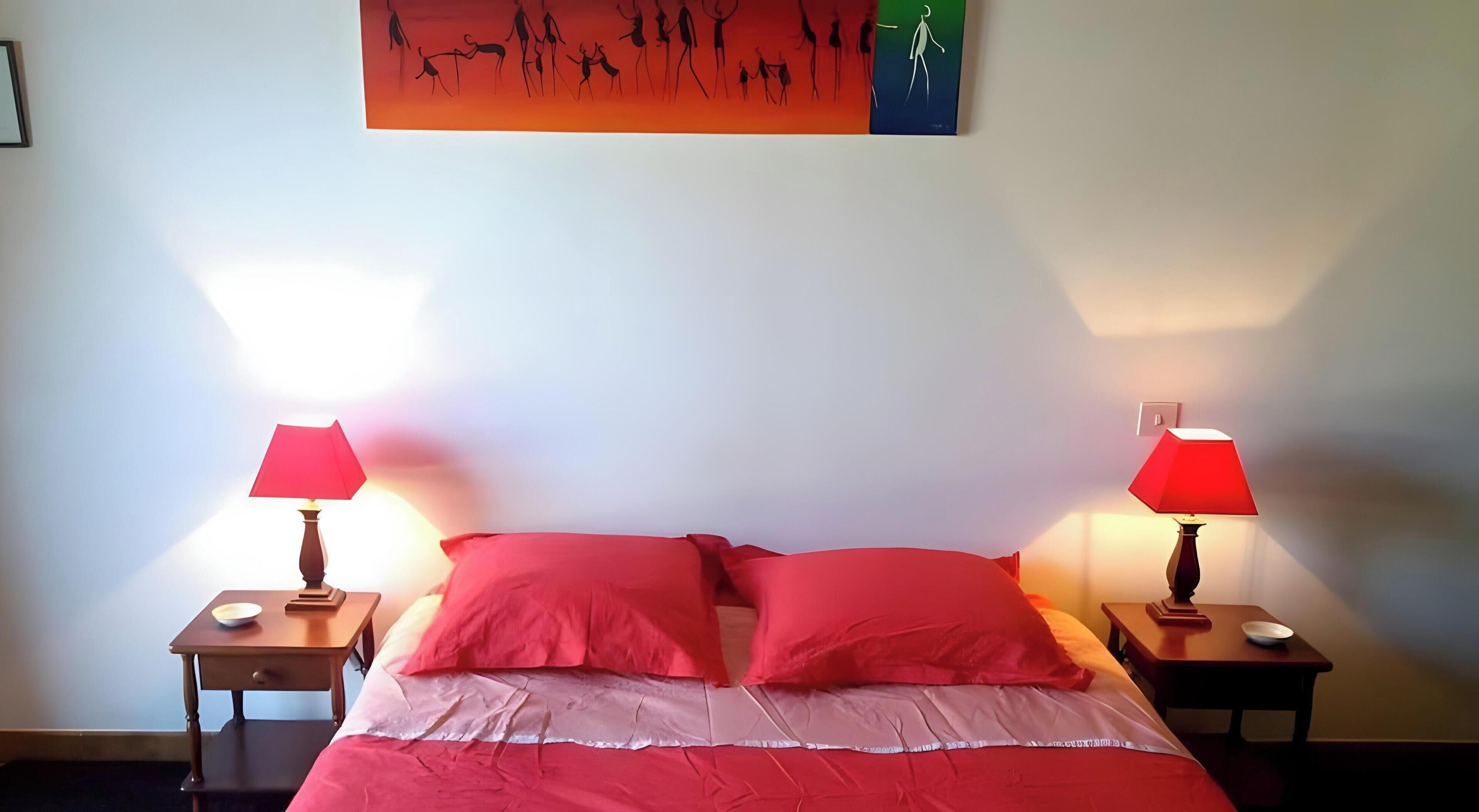 A bed with red bedding, two bedside tables with lamps, and a wall art piece above the bed.