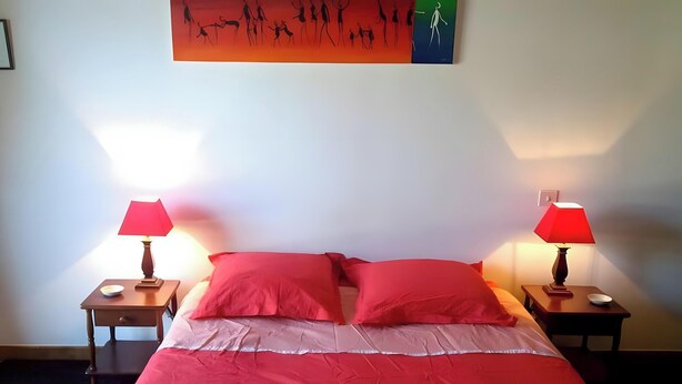 A bed with red bedding, two bedside tables with lamps, and a wall art piece above the bed. - Quiet Orchard Retreat 10 Minutes from the Beach (Quiberon)