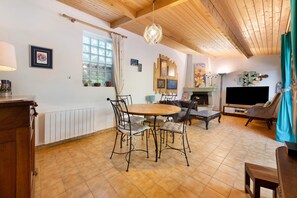 Un accogliente soggiorno con soffitto in legno, camino, zona pranzo con tavolo e sedie rotonde e televisore.